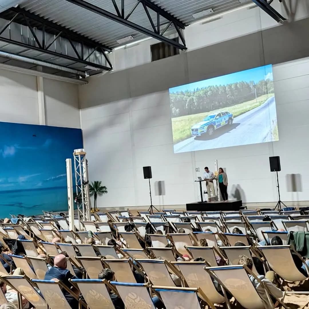 Konferens i hallen med storbildsskärm, scen och solstolar i biosittning