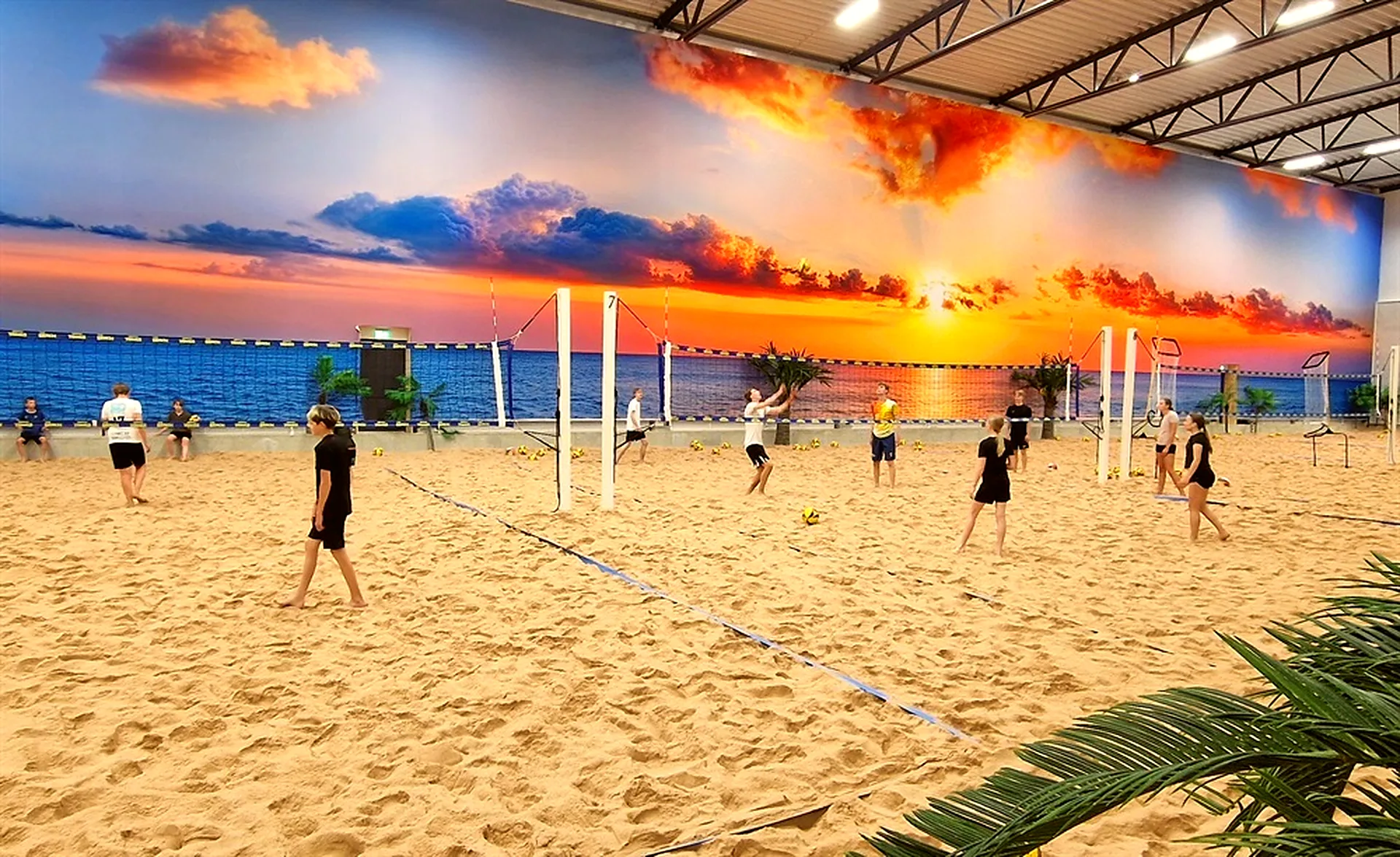 Ungdomar spelar beachvolley i sanden framför solnedgångsväggen på The Beach